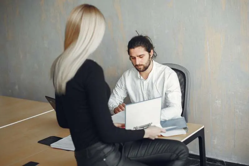 Manager expliquant une mission à un collaborateur avec une fiche de critères et un plan de suivi.