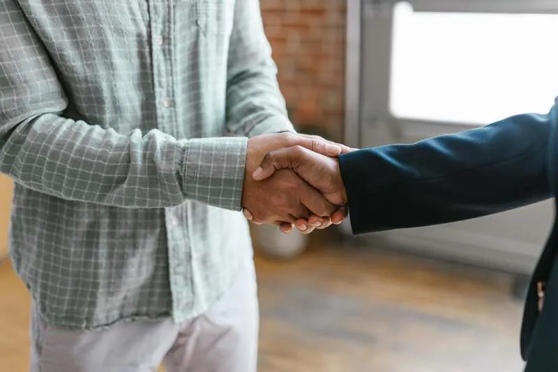 Équipe commerciale échangeant avec des clients fidèles autour d'un tableau de suivi et de café.